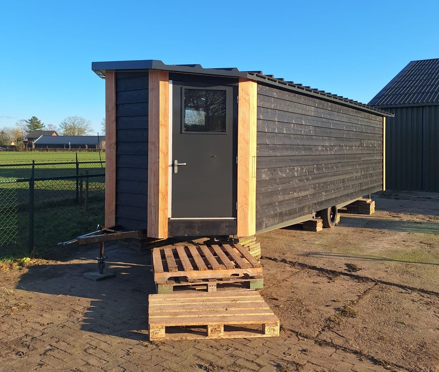 Donkere houten unit met lichte houten hoekstaanders op een onderstel, bij een boerenerf